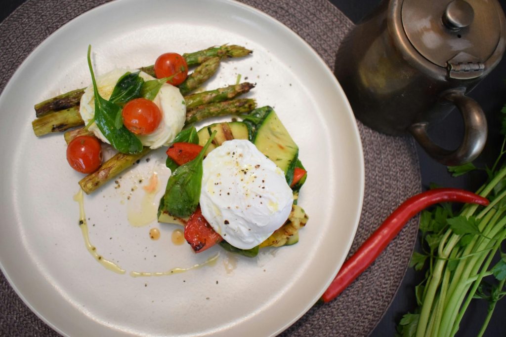 Un délicieux petit-déjeuner composé d'un œuf poché, d'asperges et de légumes, servi dans une assiette en céramique.